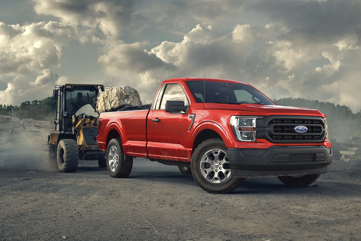 Red 2023 Ford F-150 towing a tractor.