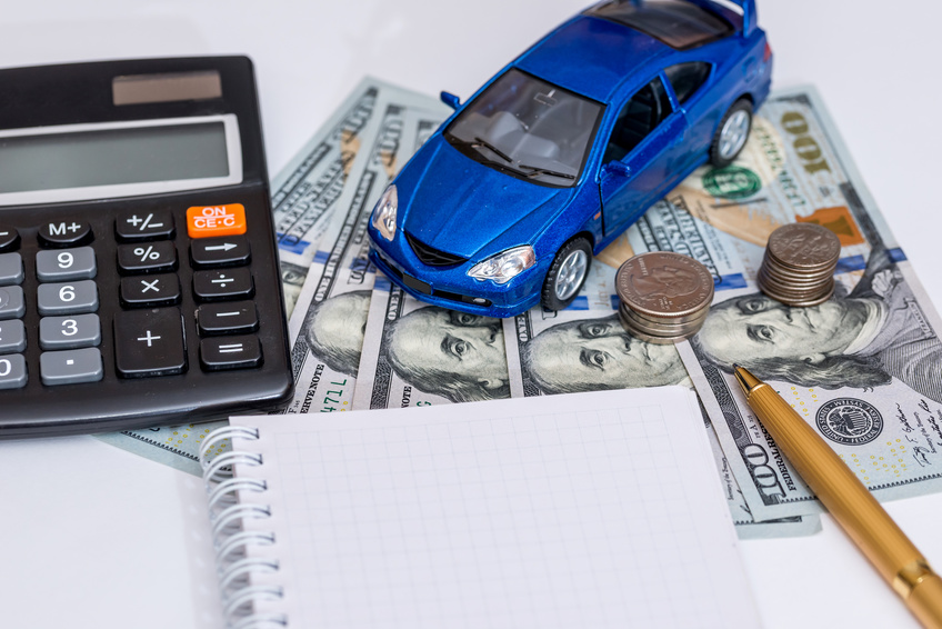 Image of a blue toy car, dollar bills, and a notepad spread out on a table.