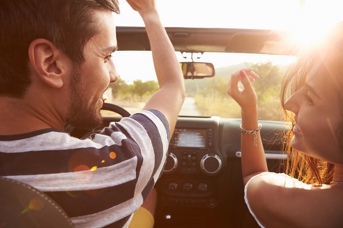 Image of a young couple driving into the sunset on a country highway.